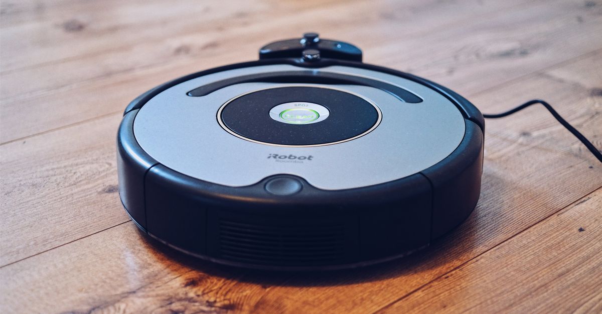 Robot odkurzający stoi na drewnianej podłodze, podłączony do przewodu zasilającego.