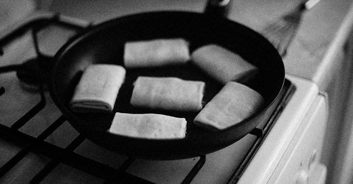 Czarna patelnia żeliwna z rolkami ciasta stoi na palniku gazowym kuchenki, zdjęcie czarno-białe.