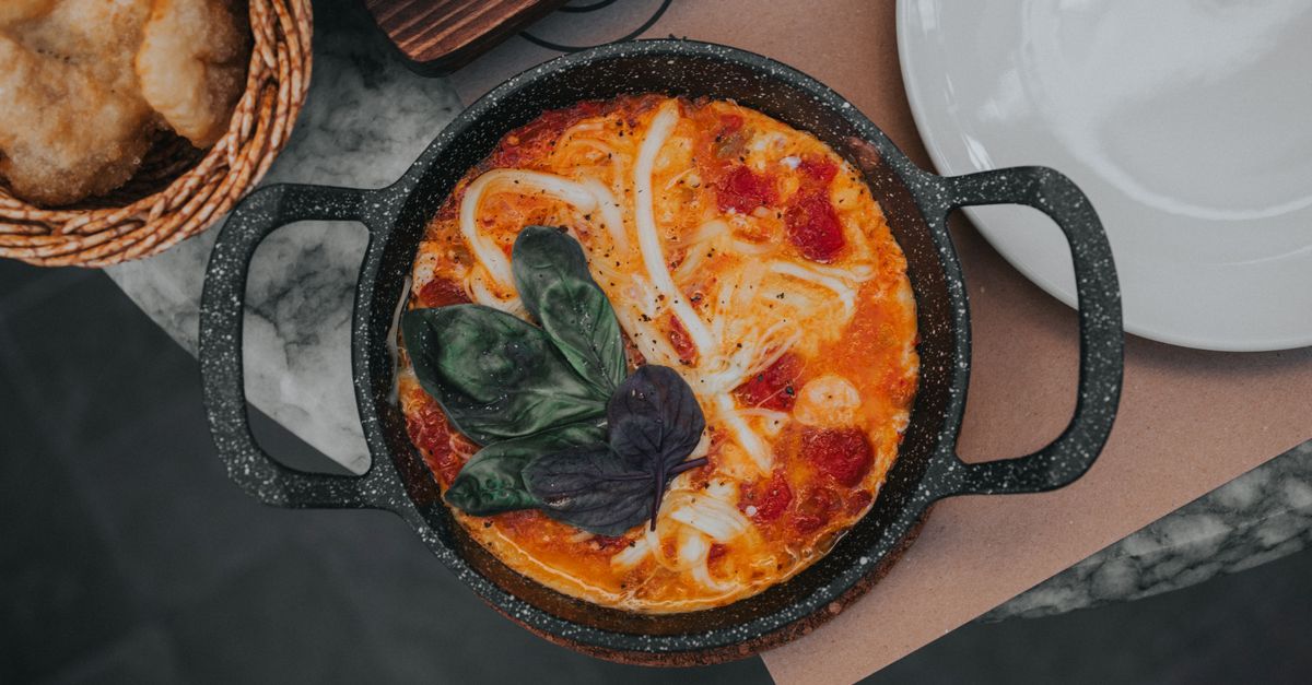 Pizza z serem mozzarella i liśćmi bazylii pieczona w małym czarnym żeliwnym naczyniu na blacie z marmuru.
