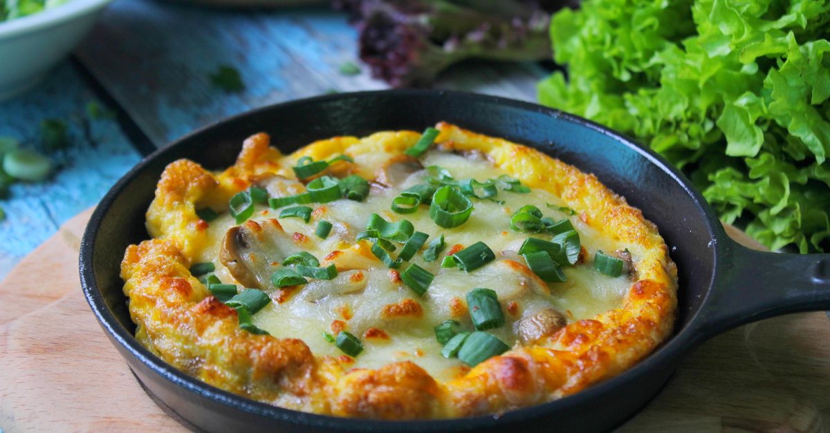 Puszysty omlet zapiekany w żeliwnej patelni, posypany serem i posiekanym szczypiorkiem, podany obok świeżej sałaty.