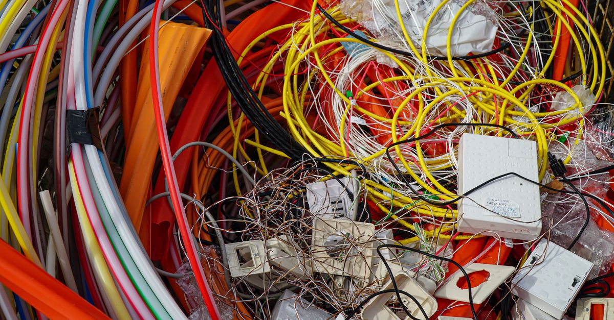 Stos splątanych kolorowych kabli i starych elementów elektronicznych w pojemniku na elektrośmieci.