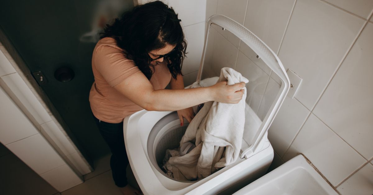 Kobieta pochylona nad pralką wyjmuje z bębna białe ręczniki podczas prania w domowej łazience.