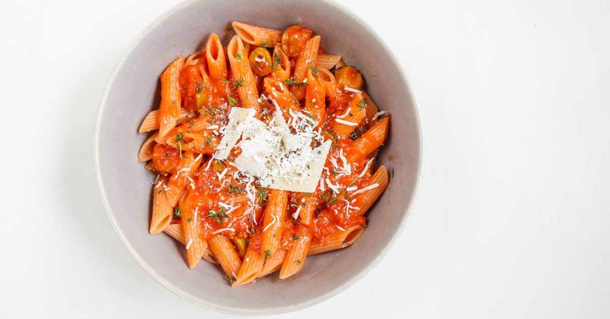Miska penne w sosie pomidorowym posypana startym parmezanem, widziana z góry na białym tle.